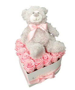 grey teddy bear with light pink ribbon sitting on the pink roses in a shape of the heart